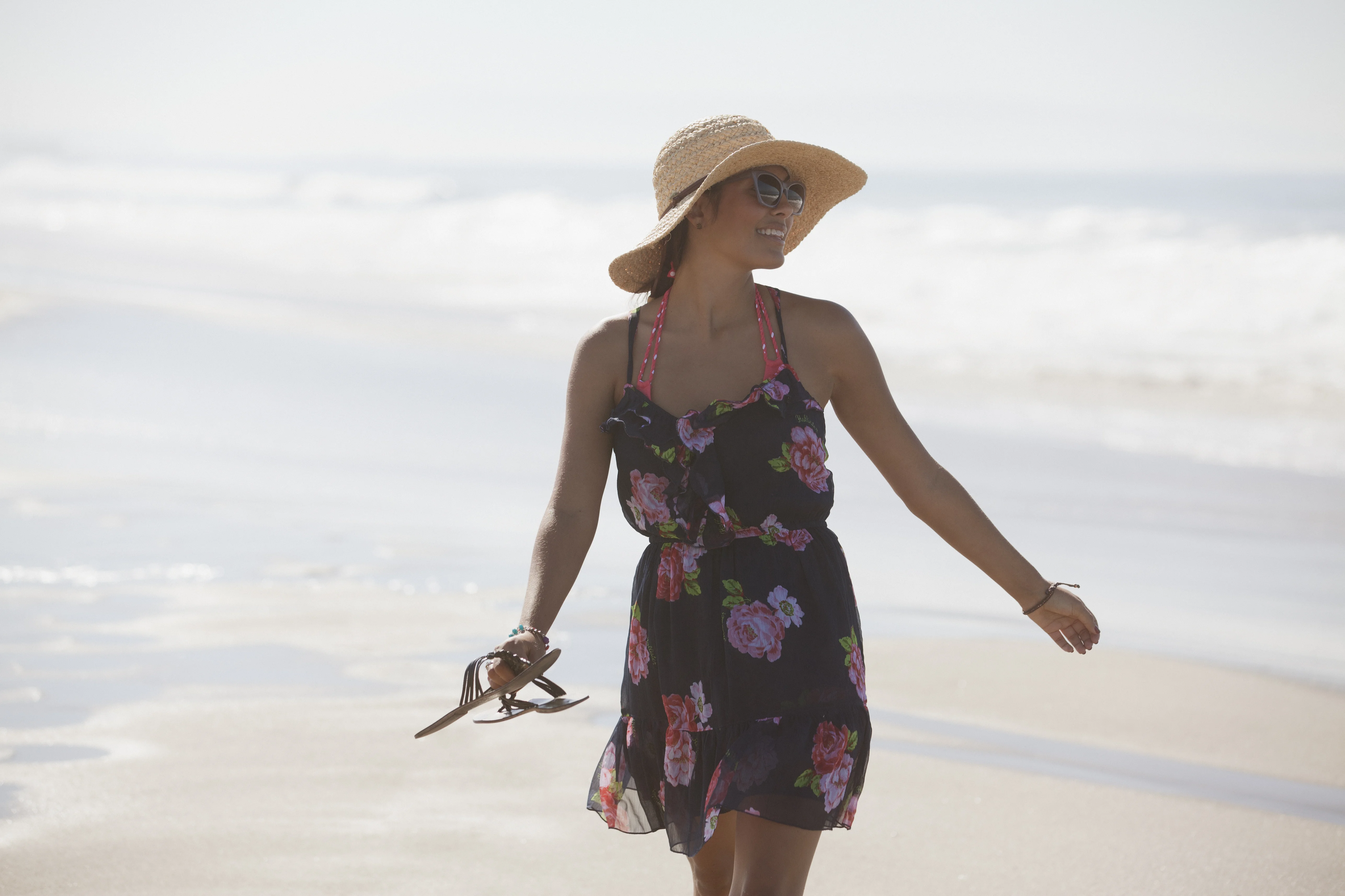 Una donna in un vestito e cappello che cammina su una spiaggia